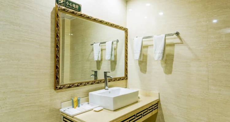 Baño de hotel limpio con espejo grande enmarcado, lavamanos tipo recipiente y toallas blancas cuidadosamente dobladas.