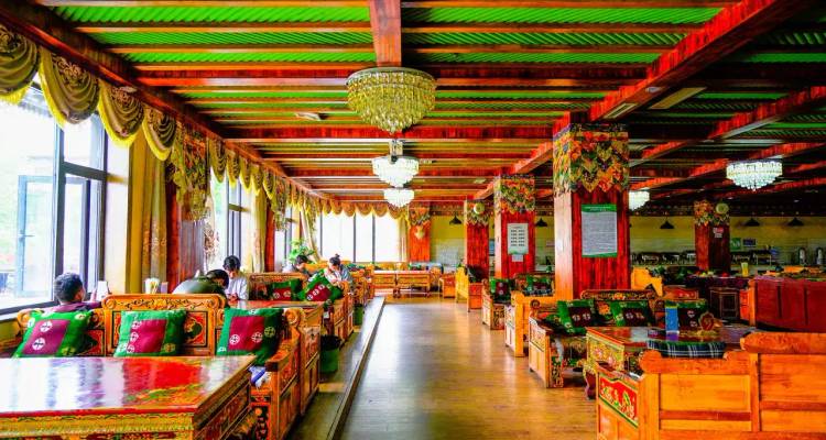 Interior de restaurante de estilo tibetano muy colorido con muebles de madera tallada, lámparas de araña y clientes comiendo.
