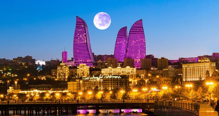 Paisaje urbano de Bakú con edificios iluminados y luna llena.