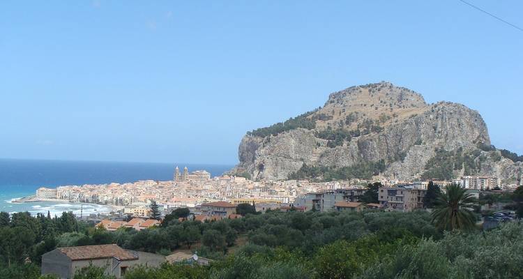 Vue panoramique d'une ville côtière avec une colline rocheuse et la mer en arrière-plan.