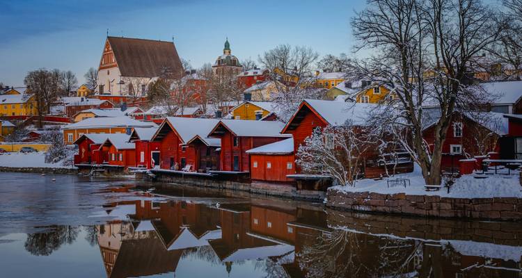 Traditional wooden houses by a frozen river with a church in the background.