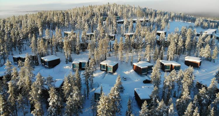 Aerial view of snowy forest with scattered cabins in the mountains.