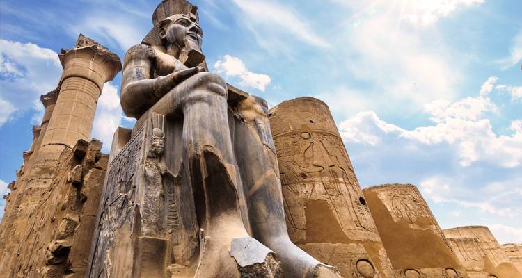 Estatua de un faraón frente a ruinas de un templo.