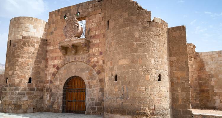 Estructura de piedra antigua con una puerta de madera y torres cilíndricas.