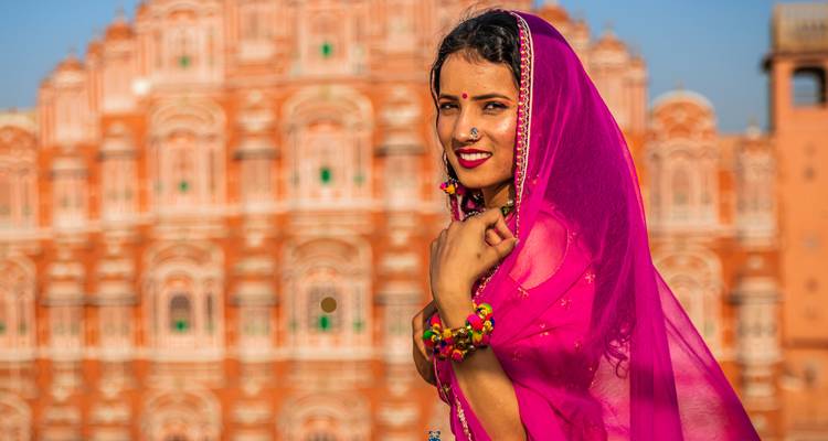 Femme en tenue traditionnelle posant devant un palais rose.