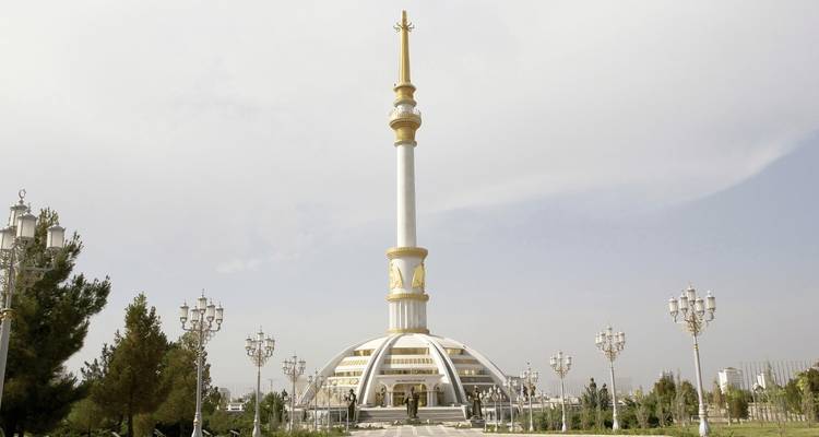 Monumento con aguja dorada y base circular ubicado en un área ajardinada.