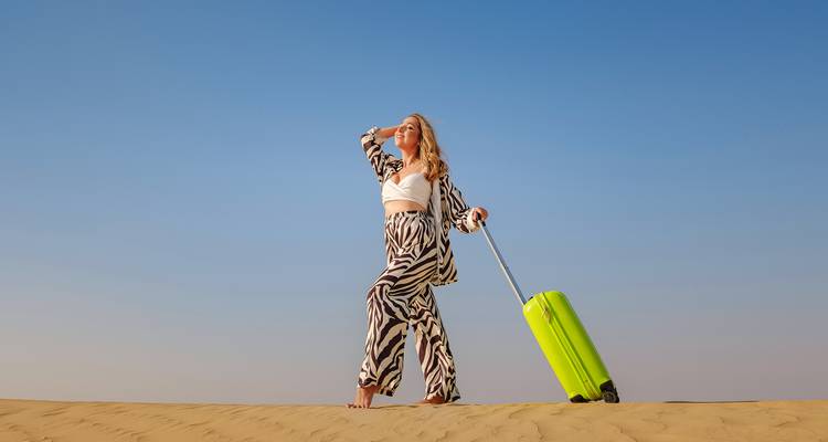 Une femme avec une valise posant en tenue de désert sur des dunes de sable.