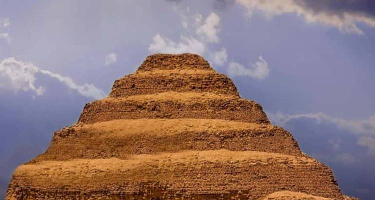 Dramatische Froschperspektive der Stufenpyramide von Djoser vor einem stimmungsvollen Himmel mit vereinzelten Wolken.
