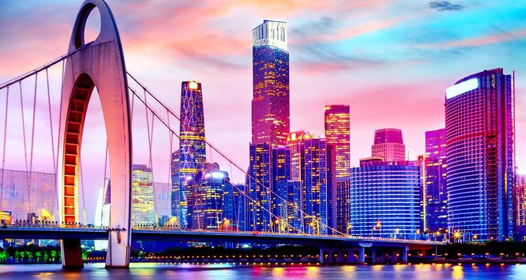 Modern cityscape with a bridge and colorful lights at sunset.