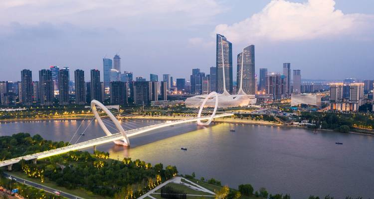 A modern skyline with a futuristic bridge over a river during the evening.