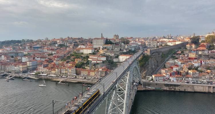Panoramische Luftaufnahme von Portos terrakottafarbenen Dächern und einer Metrobahn, die die Dom Luís I Brücke über den Douro überquert.