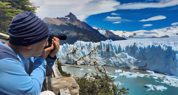 El fotógrafo apunta su cámara hacia la imponente pared de hielo del Glaciar Perito Moreno desde una plataforma de observación de madera.