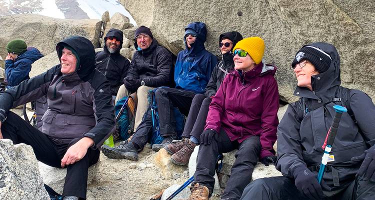 Los trekkers se acurrucan entre rocas de granito llevando chaquetas y gorros de lana mientras descansan durante una caminata de gran altitud.