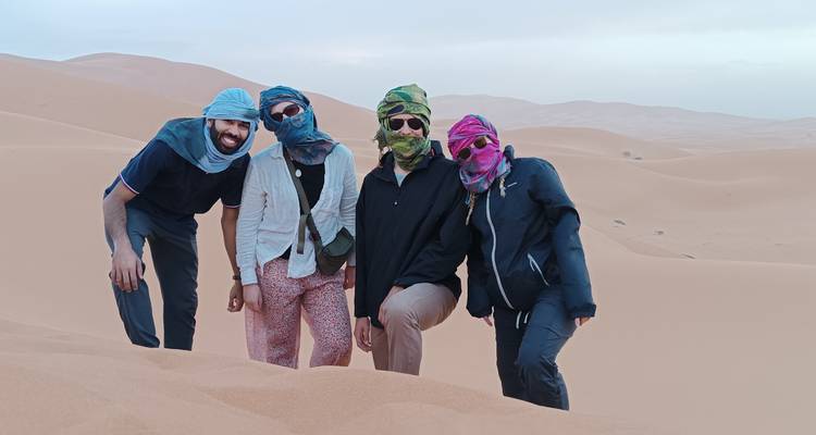 Vier mensen poseren op zandduinen met sjaals op hun hoofd.