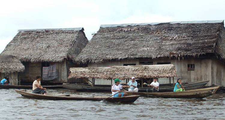 People in canoes next to traditional wooden houses on the river