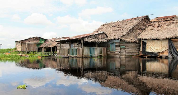 Riverside huts reflected in calm water under a clear sky