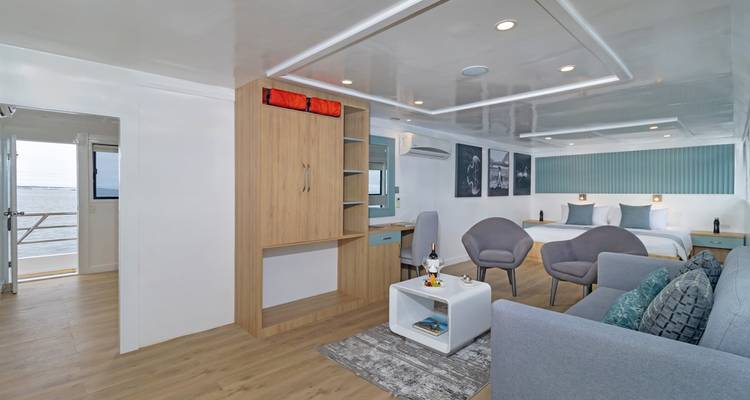 Spacious stateroom on the yacht with twin beds, seating area and balcony view of the sea.