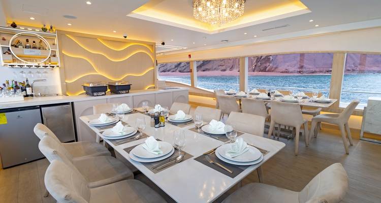 Elegant dining room on board with set tables, chandelier and ocean views through panoramic windows.