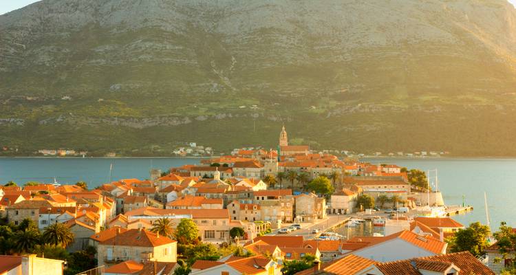 Golden light bathes Korčula’s peninsula town backed by a towering mountain and blue sea.