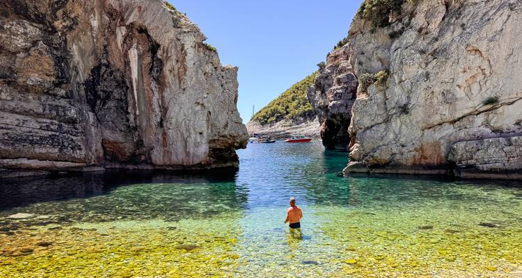 Crystal clear cove at Stiniva Beach framed by towering cliffs with a lone swimmer.