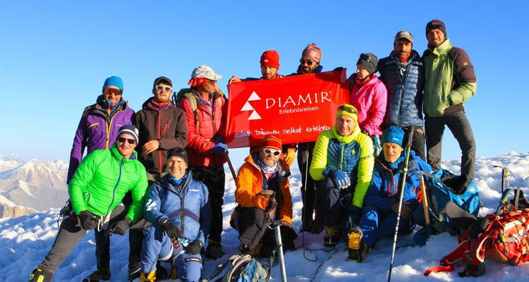 Gruppe von Bergsteigern, die auf einem schneebedeckten Gipfel mit einem Banner posieren.