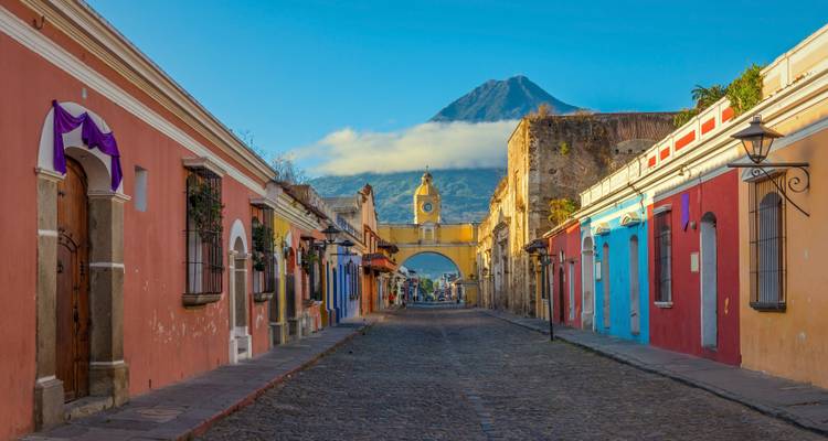 Colorful street with archway and distant volcano under clear blue sky.