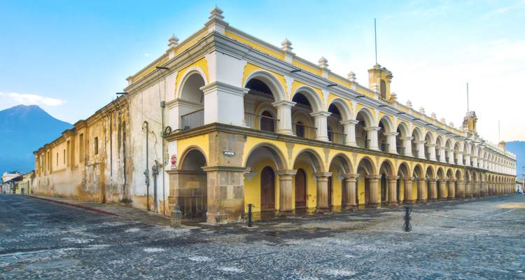 Historic building with multiple arches and a distant volcano in the background.