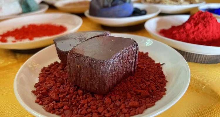 De petits plats contenant des pigments minéraux aux couleurs vives et un bloc de teinture rouge sur une table