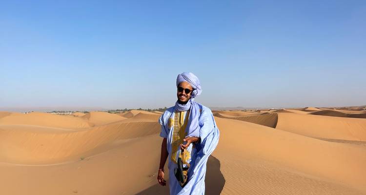 Personne en tenue traditionnelle debout dans le désert.