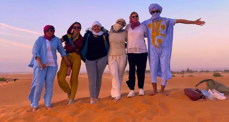 Group of people wearing colorful attire posing on sand dunes.