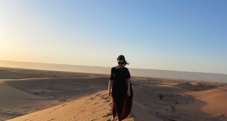 Persoon die bij zonsondergang op een zandduin loopt.