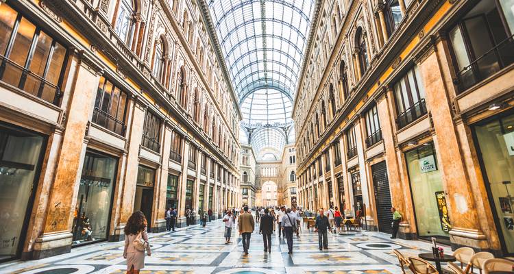 Bustling interior of Galleria Umberto I with a soaring glass roof and marble floor as shoppers stroll through.