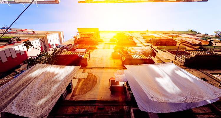 Upward alley view with laundry hanging from balconies illuminated by warm sunset light between tall buildings.