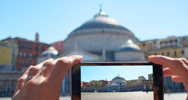 Hands holding a smartphone to photograph Piazza del Plebiscito with the basilica framed on the screen.