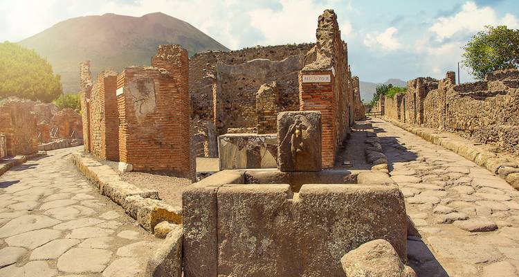 Sun-lit ruins of Pompeii with Mount Vesuvius rising in the hazy background.
