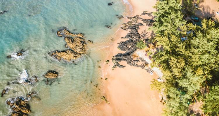 Luchtfoto van een afgelegen strand met rotsen en weelderige begroeiing.