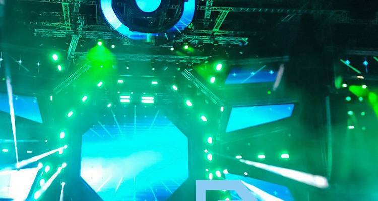 Indoor electronic music festival stage with green lasers and LED screens.