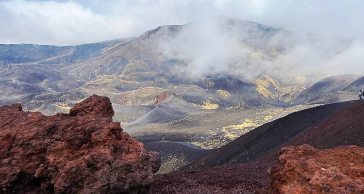 Vulkanische Landschaft des Ätna mit roten Lavasteinen, dampfenden Kratern und treibenden Wolken