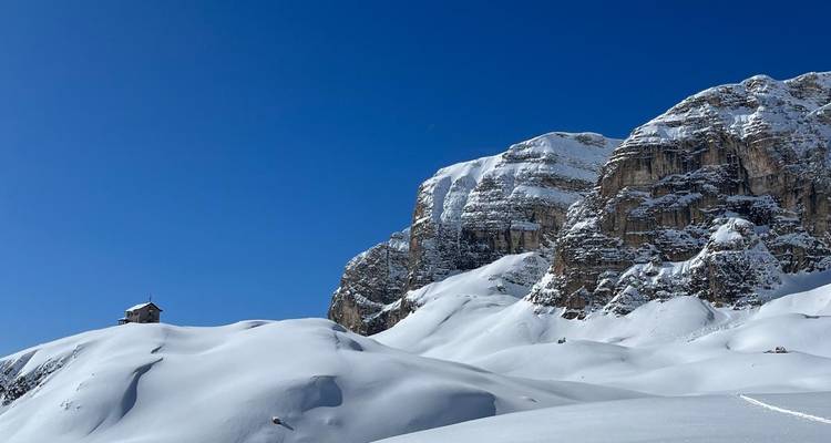 Chaîne de montagnes enneigée avec une petite maison sur une colline.