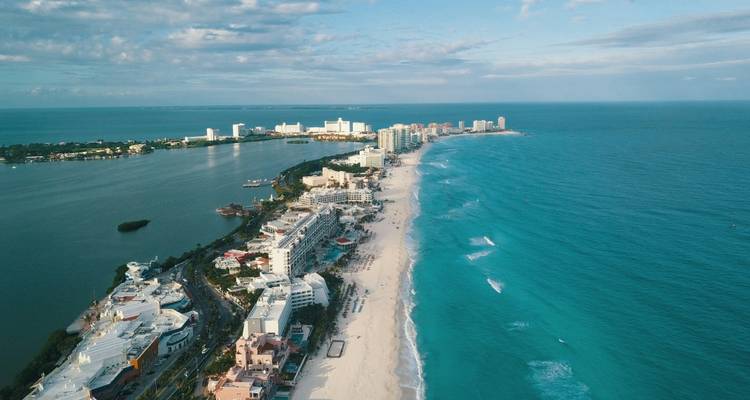 Vue aérienne d'une longue plage de sable et d'une eau bleue claire bordée d'hôtels et de bâtiments.