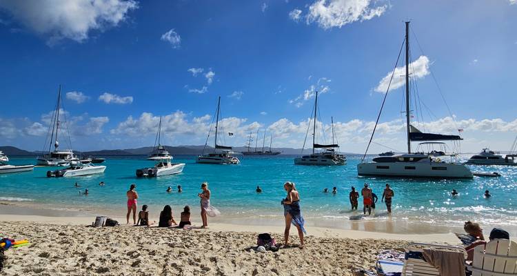 Beach with people and yachts in the blue sea.
