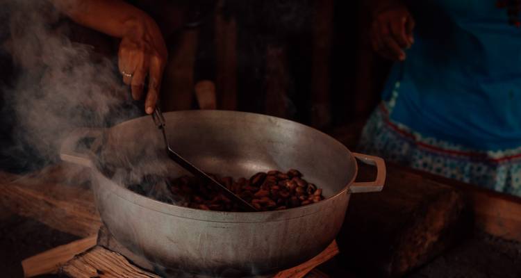 Personne faisant griller des fèves de cacao dans une casserole au-dessus d'un feu.