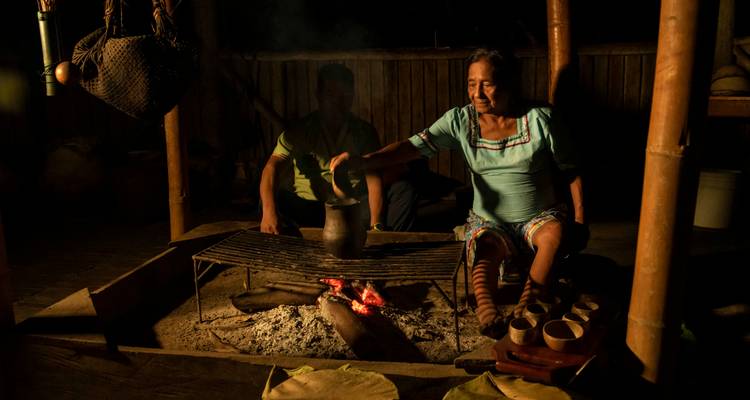 Femmes en tenue traditionnelle cuisinant sur un feu ouvert.