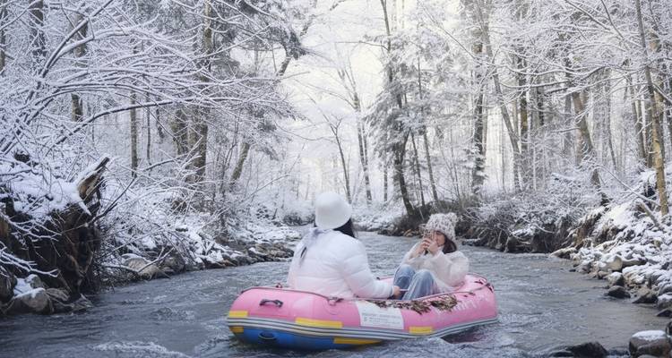Deux personnes faisant du rafting dans un paysage de rivière enneigée.