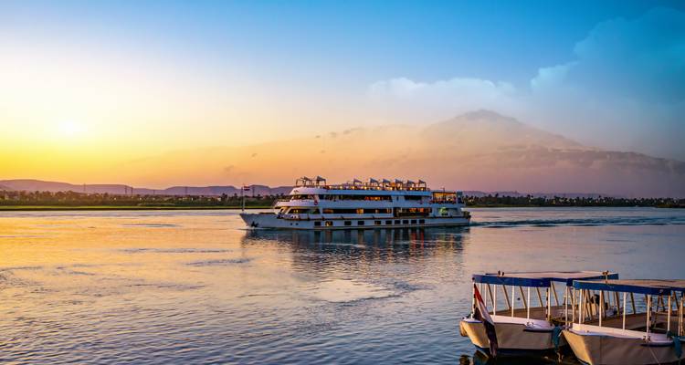 Navire de croisière de luxe naviguant sur une rivière au coucher du soleil.