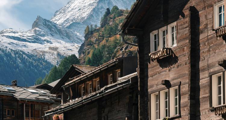 Wooden houses in a mountain village with snowy peaks.