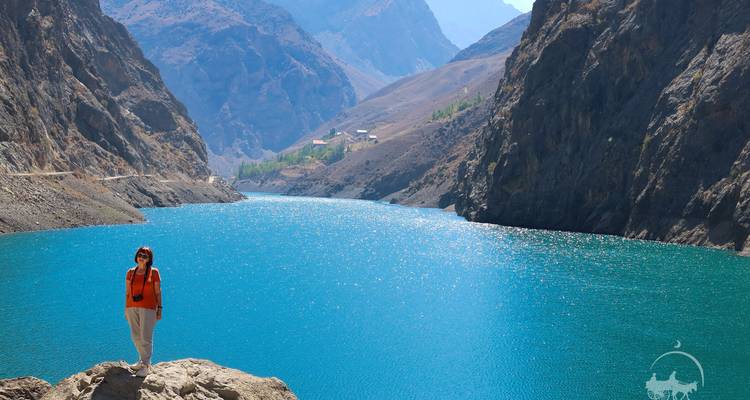 Person, die an einem türkisfarbenen See in einer bergigen Region posiert.