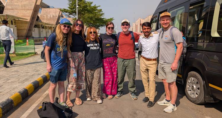Tourgroep en chauffeur glimlachen bij een zwarte minibus onder felle zon.
