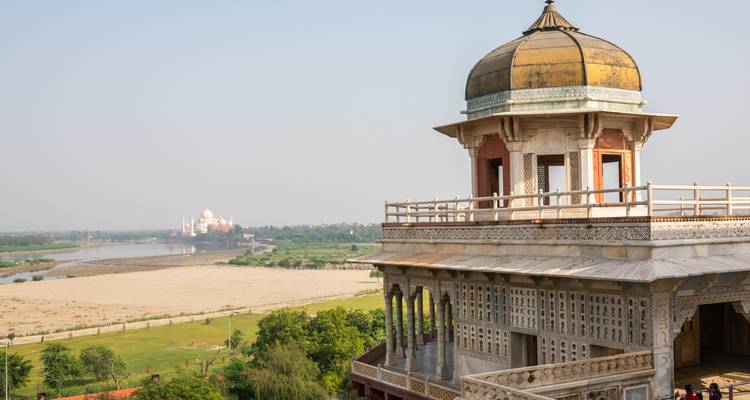 Historical building with intricate designs overlooking the Taj Mahal in the distance.