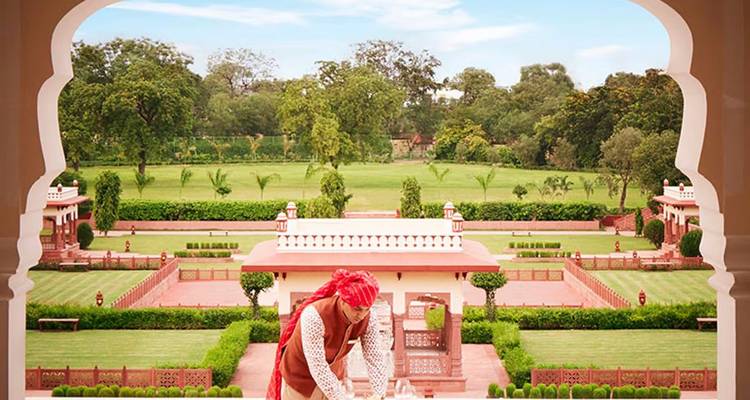 An attendant arranges a terrace setting overlooking manicured lawns framed by an ornate arch.